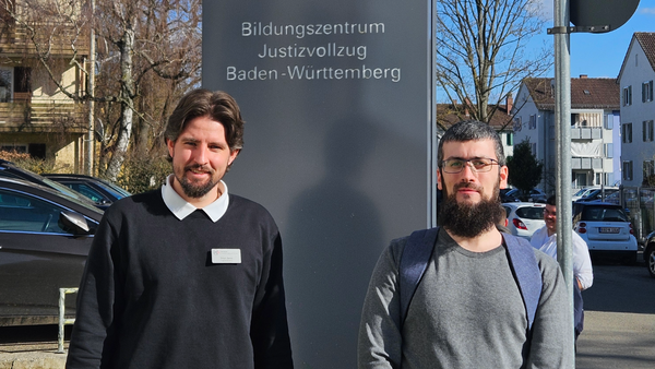 Zwei Männer stehen vor einem Schild mit der Aufschrift Bildungszentrum Justizvollzug Baden-Württemberg